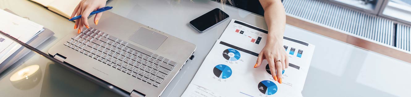 Business person looking at financial graphs in front of a laptop.